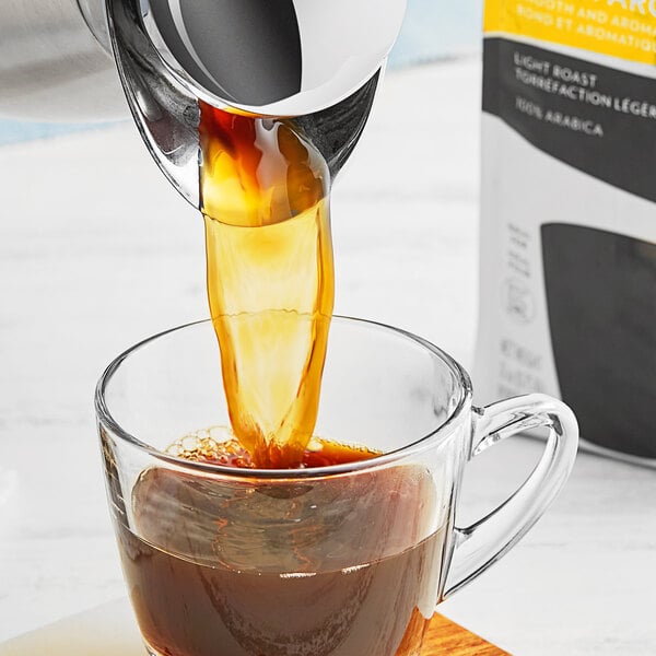 A person pouring Lavazza Gran Aroma ground coffee into a glass cup.
