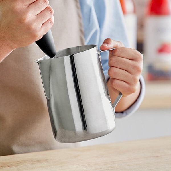 A person pouring milk into a stainless steel frothing pitcher.