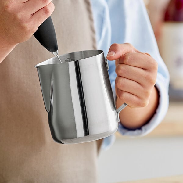 A person holding a metal frothing pitcher.