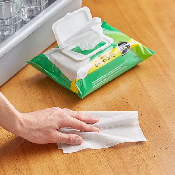 A hand using a Sani Professional multi-surface wet wipe to clean a kitchen counter.