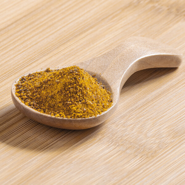 A wooden spoon filled with yellow mango powder.