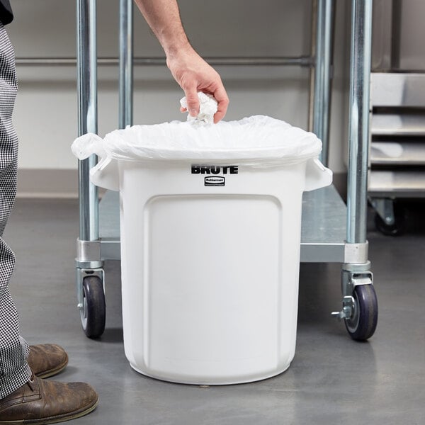 A man putting a white plastic bag in a Rubbermaid white plastic trash can.