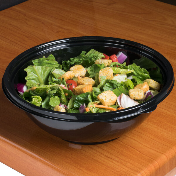 A bowl of salad in a Sabert black round bowl on a table.