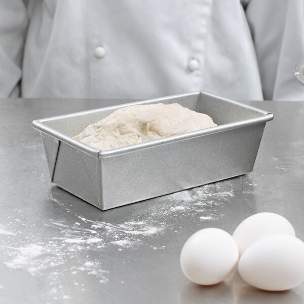 A person in a white chef's coat using a Chicago Metallic bread loaf pan to bake a loaf of bread.