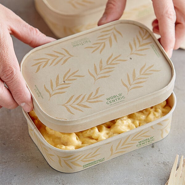 A person using a World Centric compostable paper lid to open a container of macaroni and cheese.