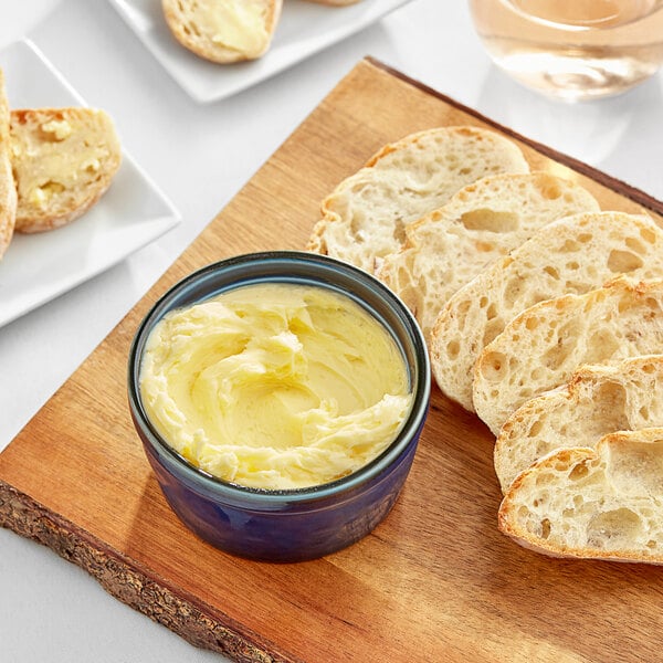 A bowl of Isigny Sainte-Mere salted butter with slices of bread on a wooden board.