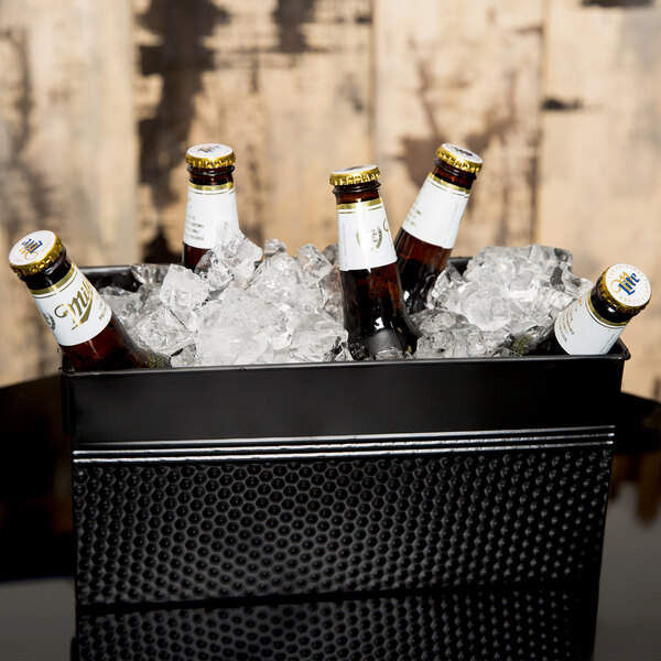 A black American Metalcraft rectangular hammered beverage tub with bottles of beer in ice.