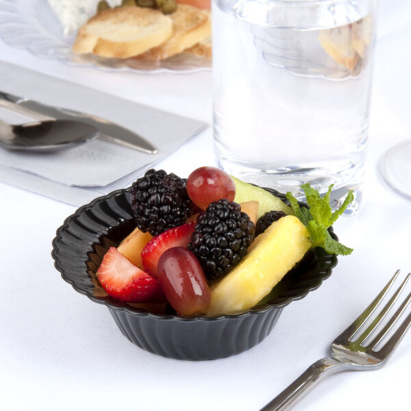 A black Fineline plastic bowl with fruit on a table in a catering event.