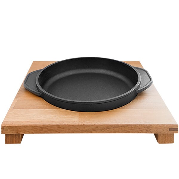 A black round pan on a wooden surface with a Mibrasa Wooden Casserole Dish Support.