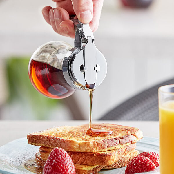 A person using a Choice glass teardrop syrup dispenser to pour syrup on a stack of french toast.