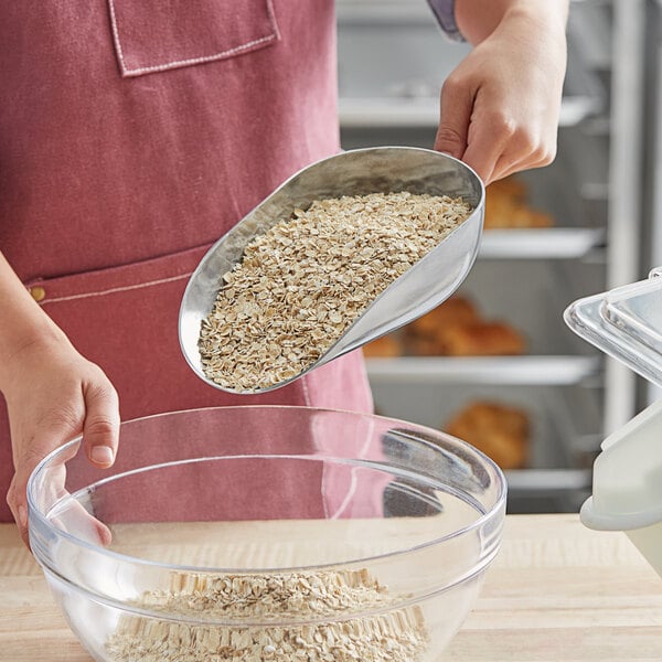 A person using a Choice aluminum scoop to pour oats into a bowl.