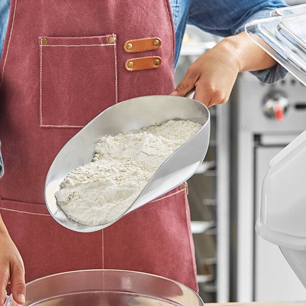 A woman in an apron using a Choice aluminum scoop to measure flour.