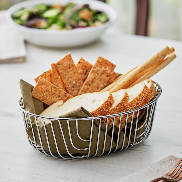 An Acopa oval chrome wire basket filled with bread and crackers.