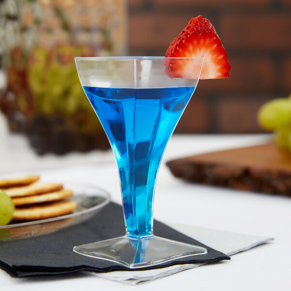 A close-up of a blue drink in a Fineline Tiny Barware clear plastic square wine glass with a strawberry on top.