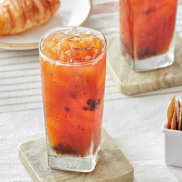 A glass of Davidson's Organic Blackcurrant Iced Tea with ice on a table with a croissant.