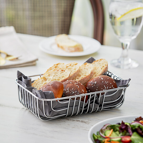 An Acopa rectangular chrome wire basket on a table with bread and salad.