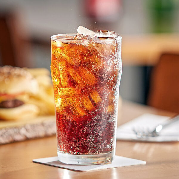 A glass of Pepsi soda with ice on a table with a burger.