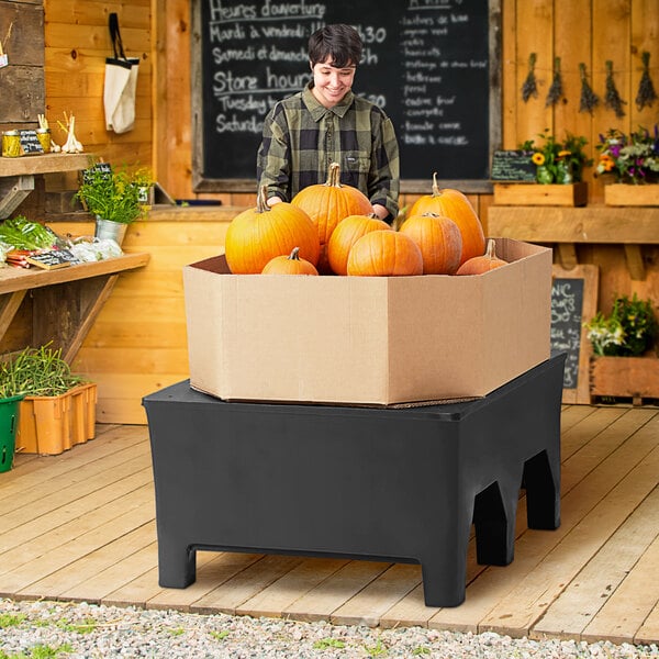 A man standing next to a MasonWays black dunnage rack holding a box of pumpkins.