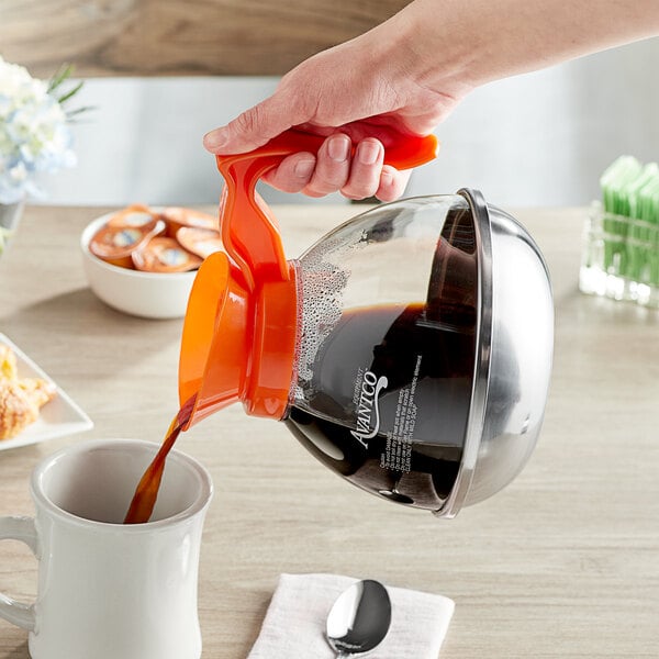 A person pouring decaf coffee into a cup from an Avantco polycarbonate coffee decanter with an orange handle.