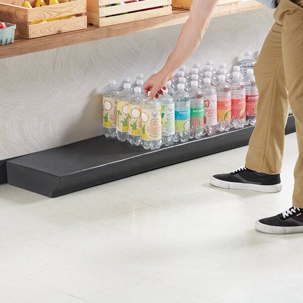 A man using a MasonWays black plastic platform to stack water bottles on a counter.