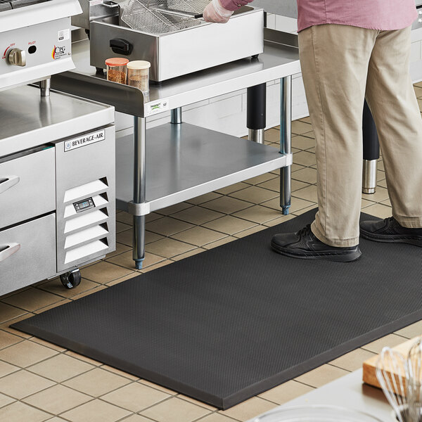 A man standing on a black anti-fatigue floor mat in a kitchen.