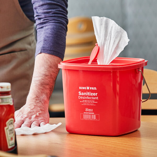A person cleaning a table with a red Noble Products sanitizing pail.