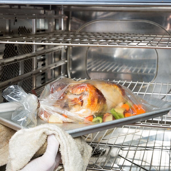 A gloved hand holding a tray with a cooked turkey in a Kenylon oven bag.