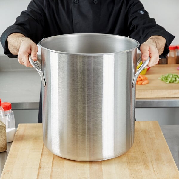 A person holding a large silver Vollrath stock pot.