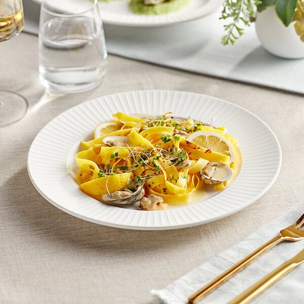 An Acopa Cordelia porcelain plate with pasta, mushrooms, and lemon.