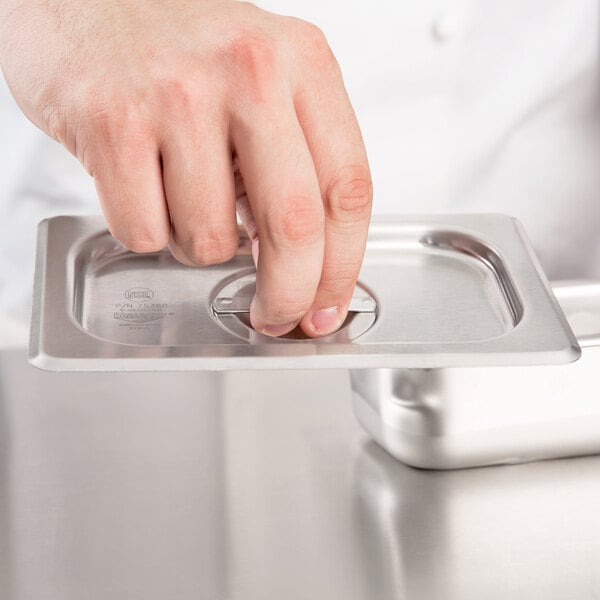 A hand using a Vollrath Super Pan V stainless steel lid to cover a metal tray.