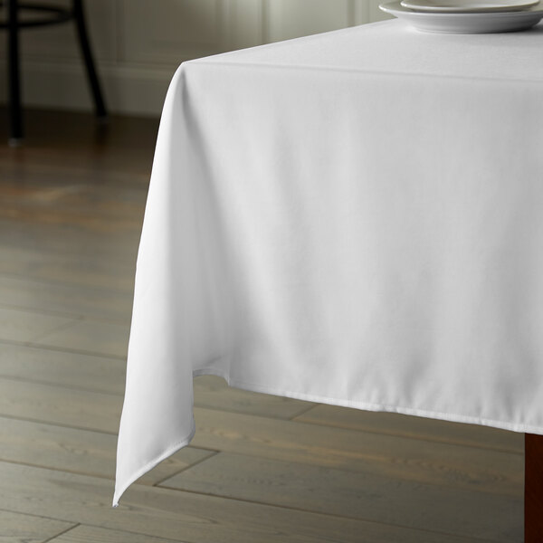 A table with a white Intedge square tablecloth on it with a plate.