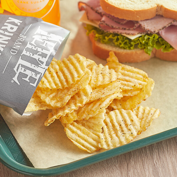 A sandwich and Kettle Brand Salt & Fresh Ground Pepper Krinkle Cut Potato Chips on a tray.