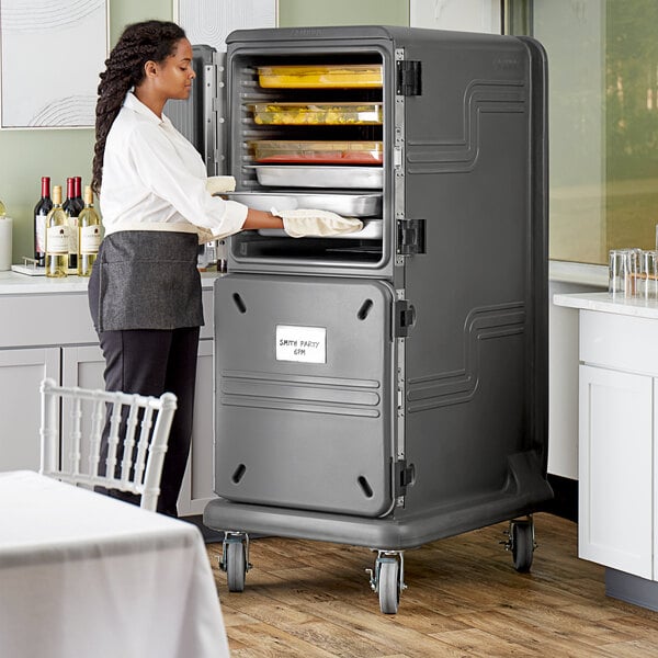A woman in a white shirt and black pants adding food to a Cambro Pro Cart Ultra tall pan carrier.
