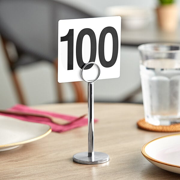 A white table number card with the number 100 in black on a metal holder.