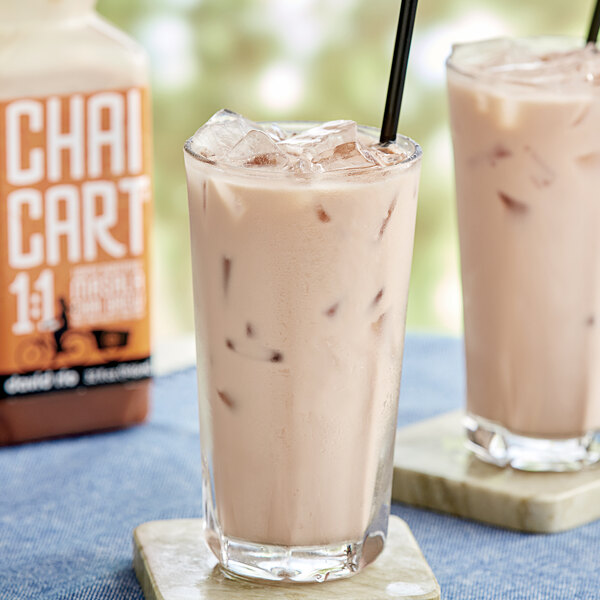 A bottle of David Rio Masala Chai concentrate on a table with two glasses of iced chai.