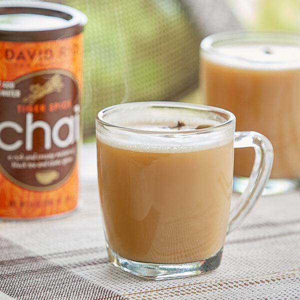 A glass mug of brown David Rio Tiger Spice Chai tea on a table with a can of tea.