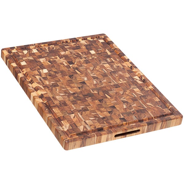 A Teakhaus end grain teakwood cutting board with juice canal and hand grips on a table.