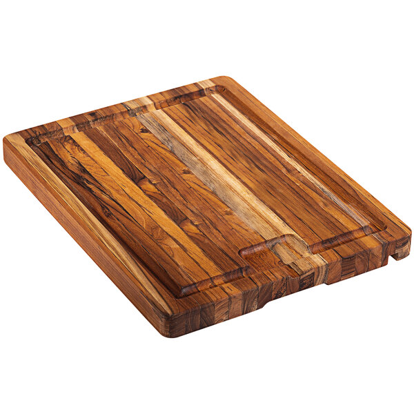 A Teakhaus edge grain teakwood cutting board with a juice canal and tablet slot on a table.