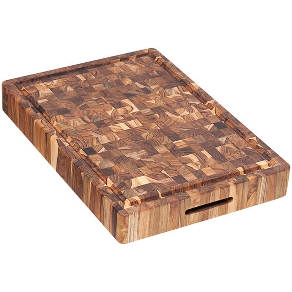 A Teakhaus end grain teakwood cutting board with hand grips and a juice canal on a table.