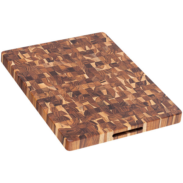 A Teakhaus end grain teakwood cutting board with hand grips on a table.