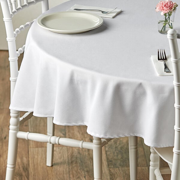 A white table with a Choice white 100% spun polyester table cover and flowers on it.
