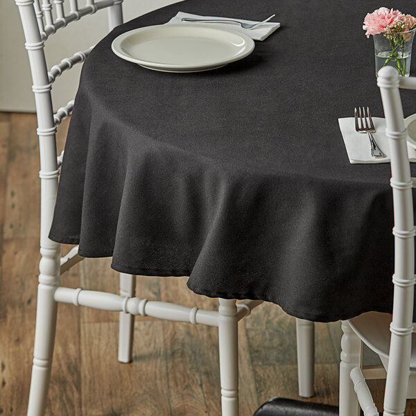A table with a black Choice cloth table cover and white chairs.