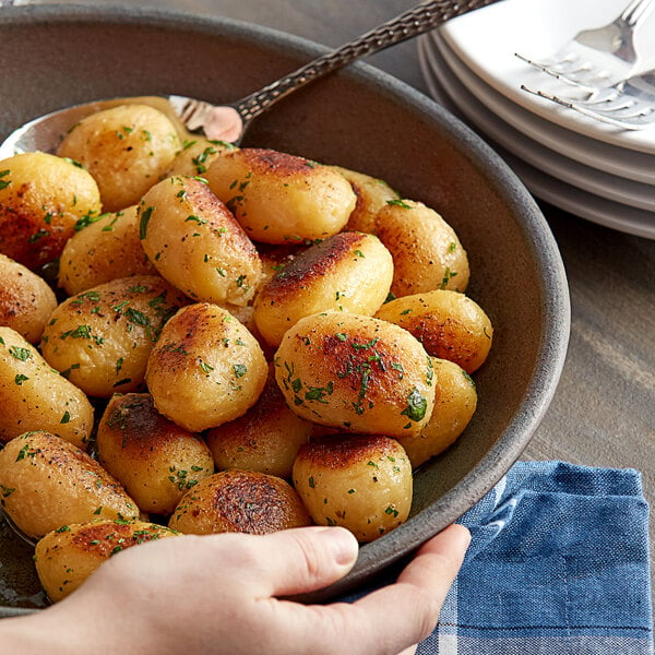 A bowl of medium whole skinless white potatoes with green leaves on top.