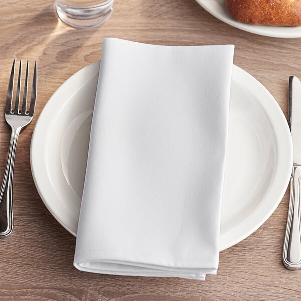A white Choice cloth napkin on a plate with a fork and knife on a wooden table.