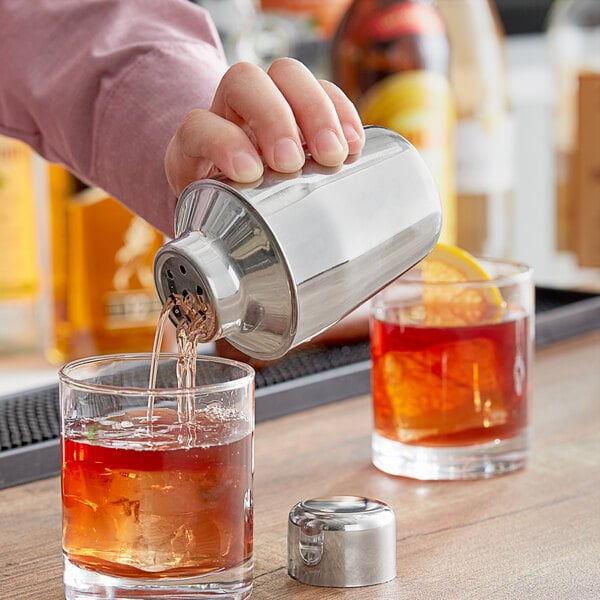 A person using an Acopa Stainless Steel Cobbler Cocktail Shaker to pour a drink into a glass.