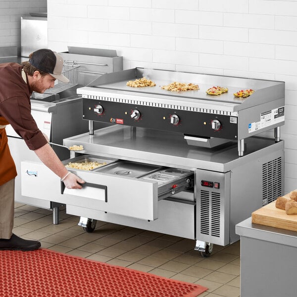 A man in an apron using a Cooking Performance Group countertop electric griddle over a refrigerated base.