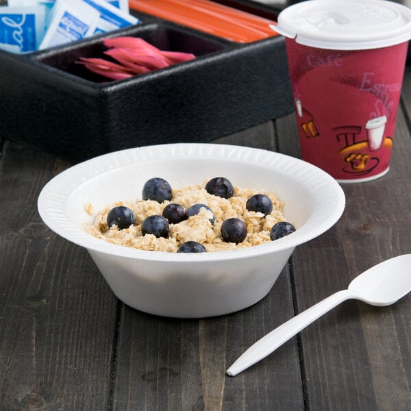 A Dart white foam bowl filled with oatmeal and blueberries on a table with a spoon.