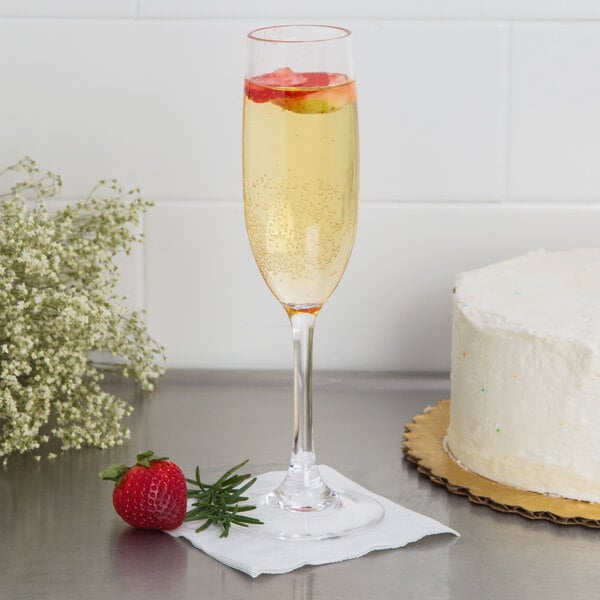 A Carlisle plastic champagne flute filled with champagne next to a cake.