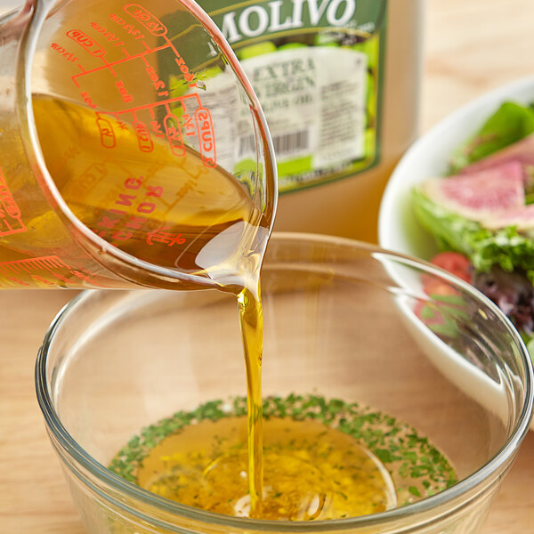 A glass bowl of Molivo Extra Virgin Olive Oil being poured over a salad.