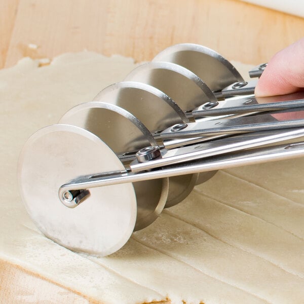 A hand using an Ateco stainless steel pastry cutter to cut dough.